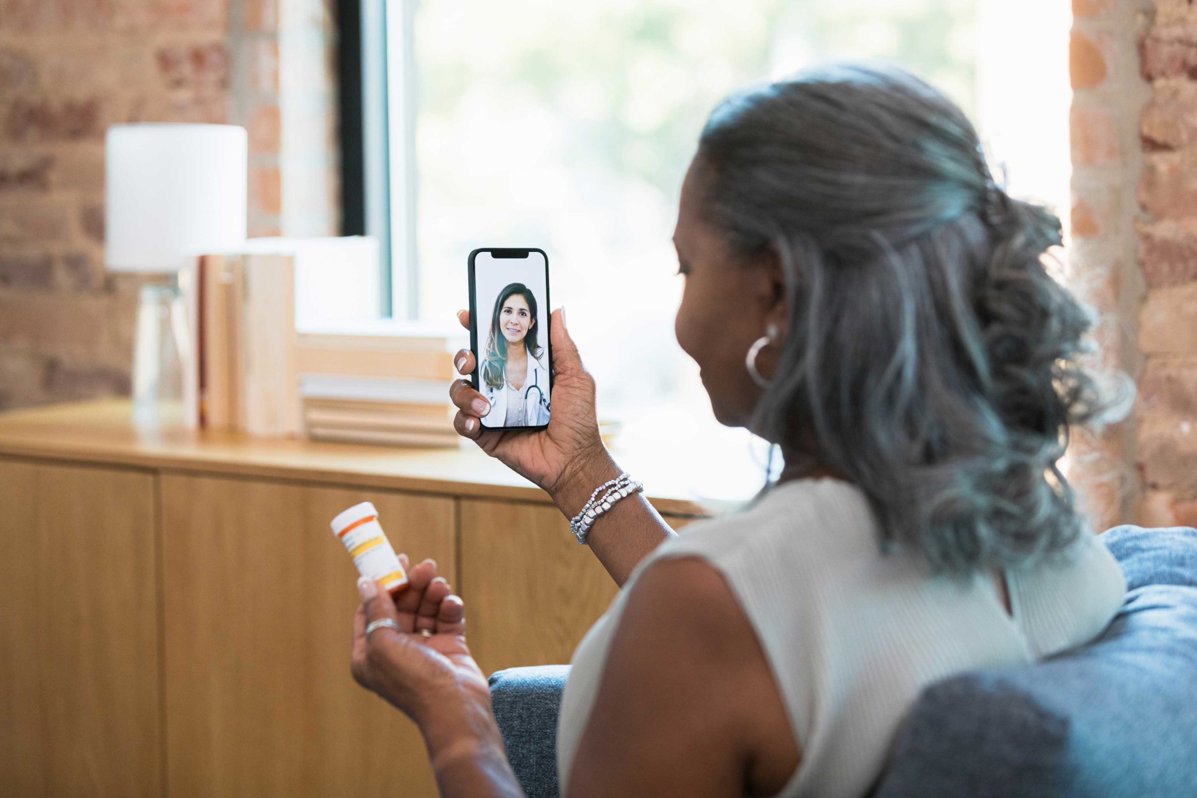 An older adult holds her medication while speaking with a doctor by video call.
