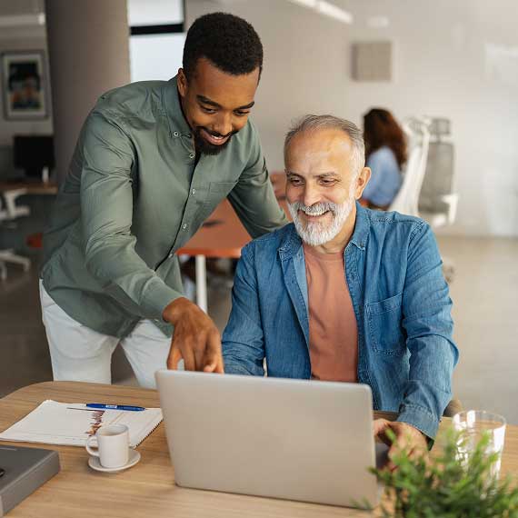 A broker helps an older adult navigate health information on a laptop.